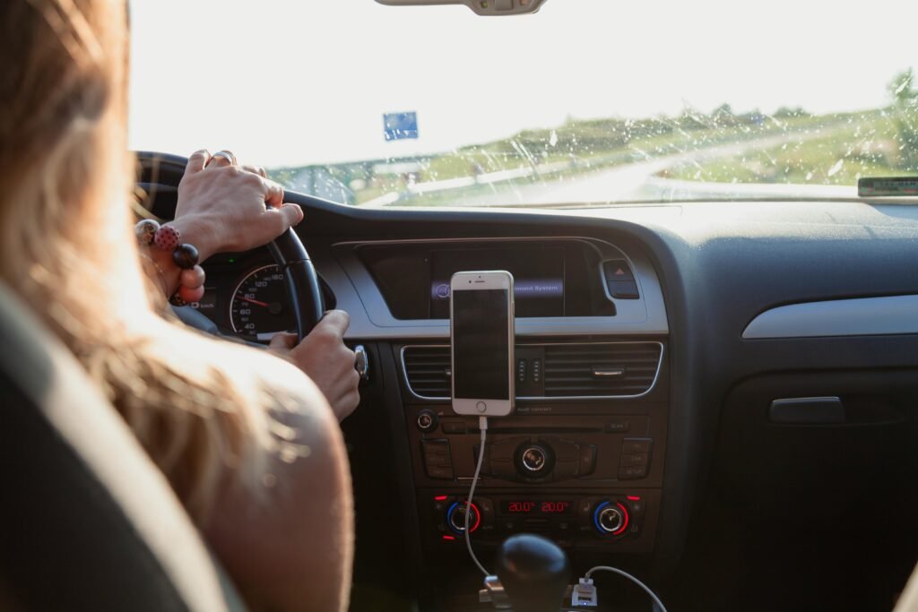 View from behind a woman driving a car on a sunny day with a phone mounted on the dashboard.