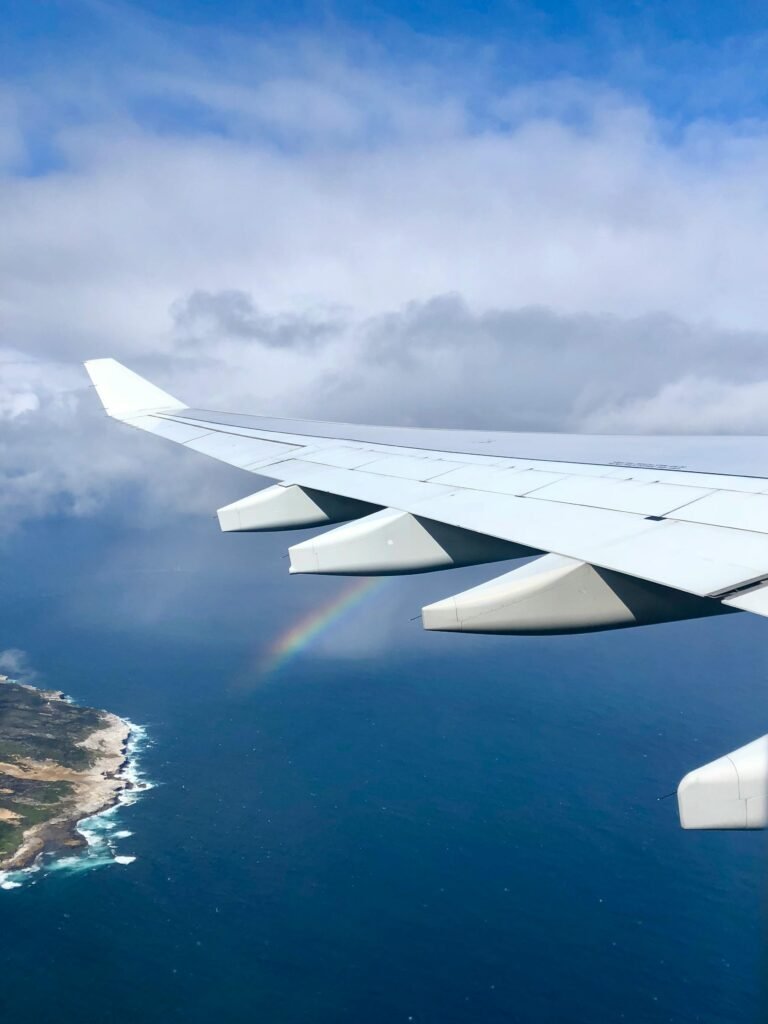 A scenic aerial view of an airplane wing over the ocean, featuring a rainbow in the sky.