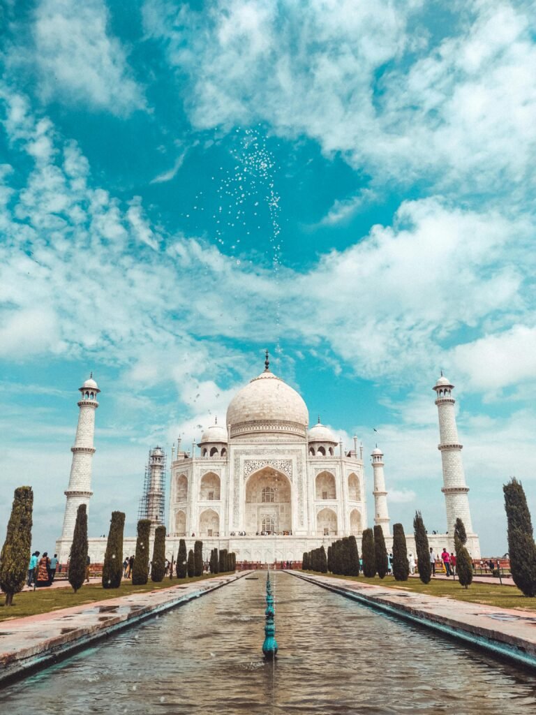 A majestic view of the iconic Taj Mahal under a bright, blue sky with clouds.