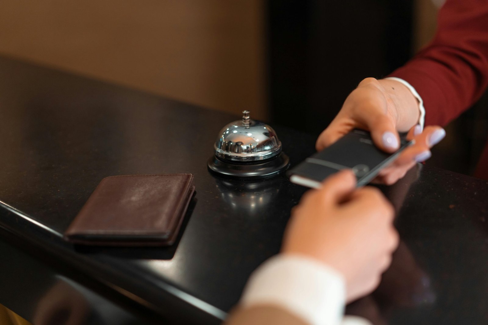 A close-up of a hotel check-in process with a smartphone and card transaction at the reception desk.